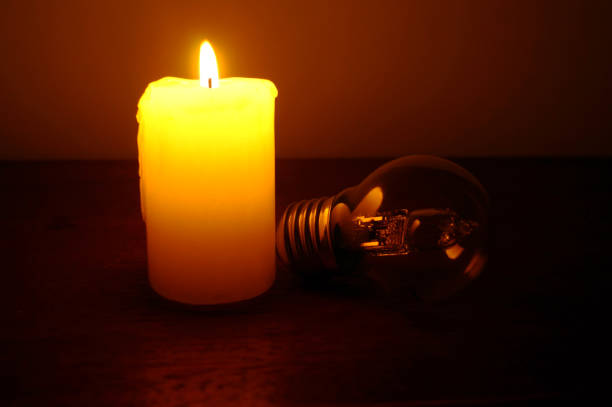 Burning candle and lamp on desktop in darkness. Troubles with electricy after storm.
