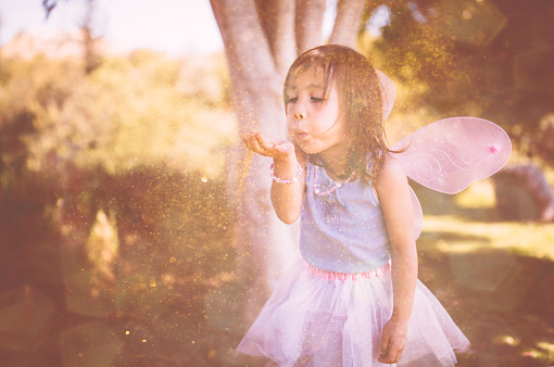 Asian girl dressed as fairy blowing glitter and having fun in the garden in spring
