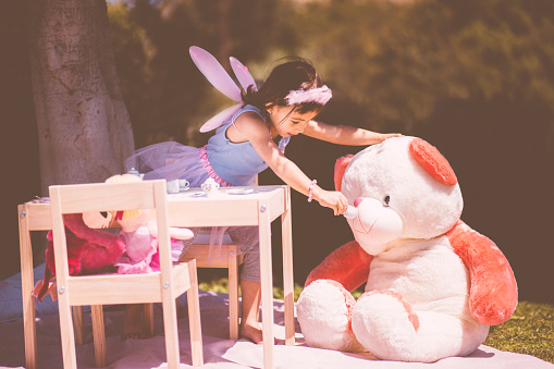 Playful little Asian girl having a tea party with stuffed toy animals in the garden