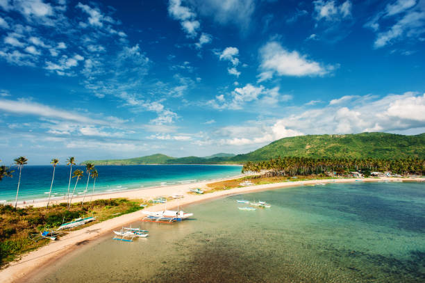 Tropical country, beach with palm trees, blue sky with clouds. Isthmus between two seas. Philippines, Palawan, Napcan beach