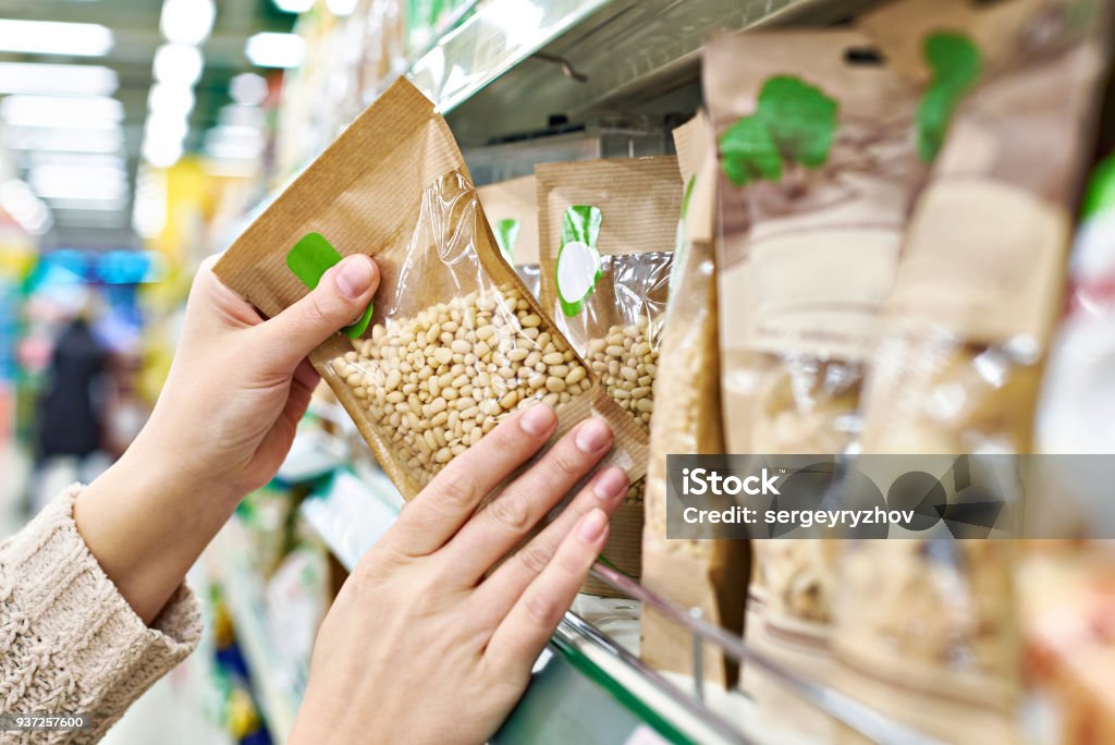 Manos con piñones de envasado en la tienda - Foto de stock de Orgánico libre de derechos