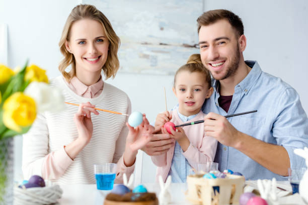istock Celebrating family with daughter coloring Easter eggs by table 937265678