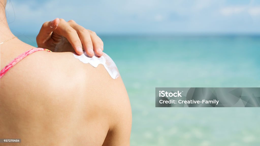 Girl applying sun lotion on the beach Girl applying sun lotion on the beach back view Suntan Lotion Stock Photo