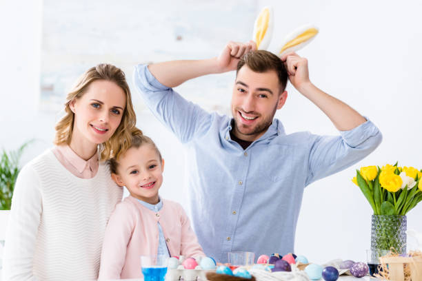 istock Happy family playing with bunny ears by table with colored eggs for Easter 937271510
