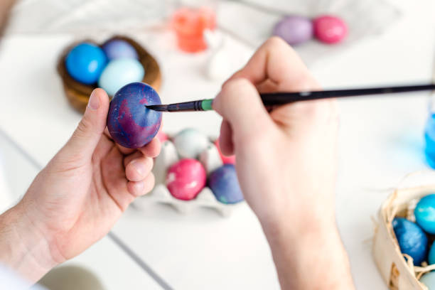 istock Man coloring Easter eggs with painting brush 937274006