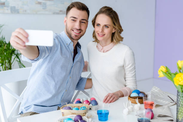 istock Young man and woman taking selfie while painting Easter eggs 937275690