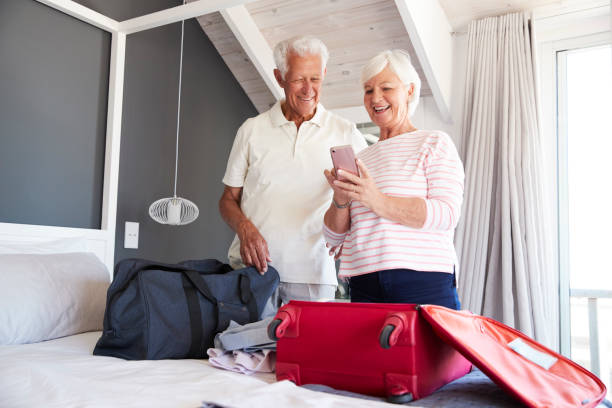 casal sênior olha móvel como eles chegaram-in para aluguer de férias - luggage packing suitcase old - fotografias e filmes do acervo