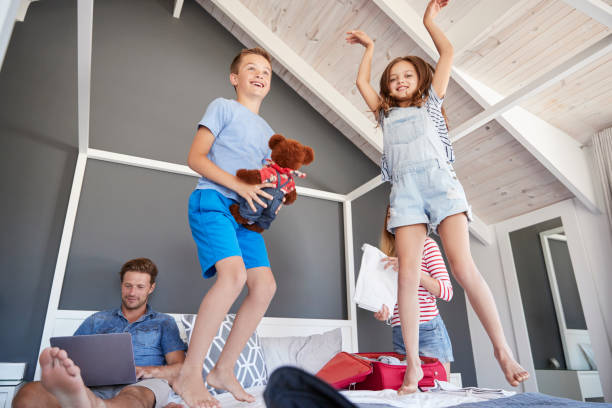 istock Excited Children Jump On Bed As Parents Pack For Vacation 937278418