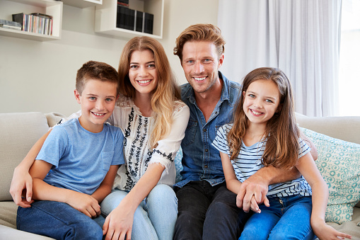 Portrait Of Smiling Family Sitting On Sofa At Home Together