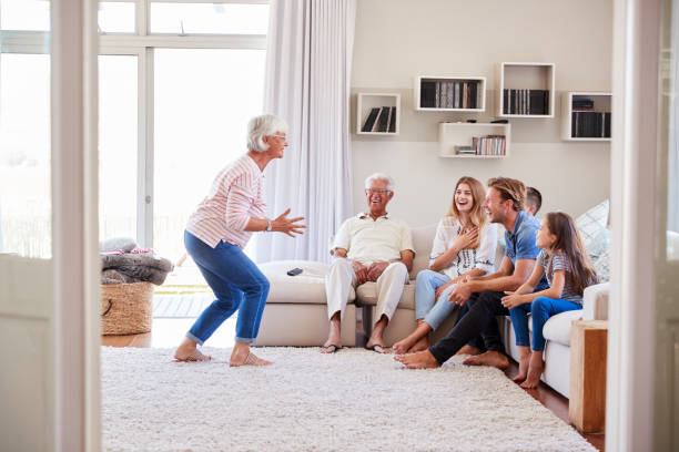 Multi Generation Family Sitting On Sofa At Home Playing Charades