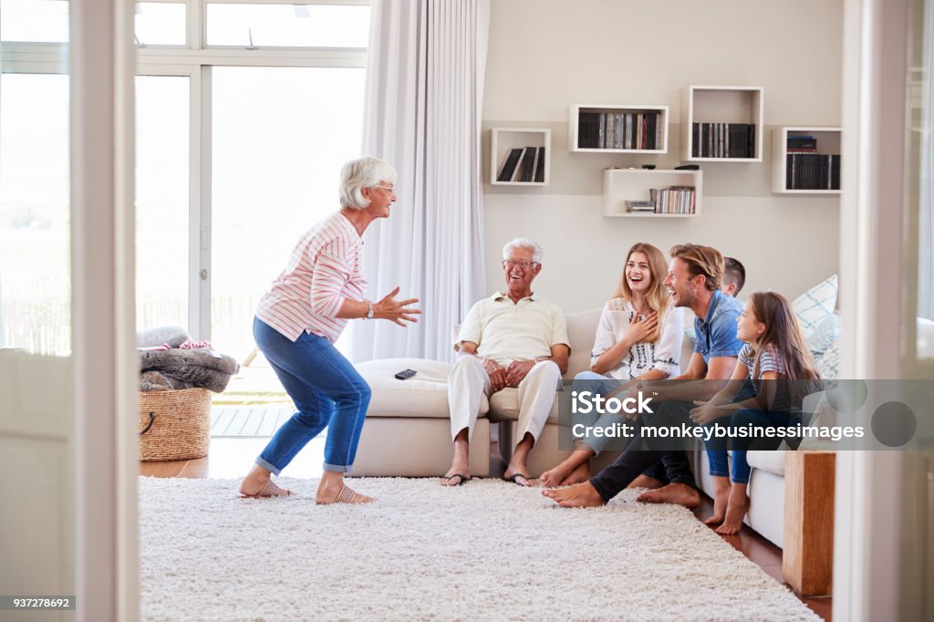 Multi Generation Family Sitting On Sofa At Home Playing Charades Family Stock Photo