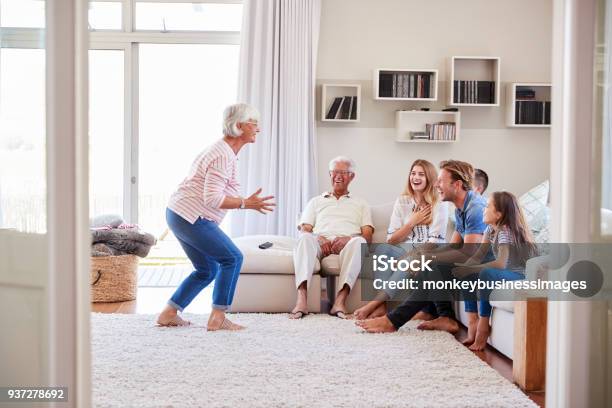 Multi Generation Family Sitting On Sofa At Home Playing Charades Stock Photo - Download Image Now