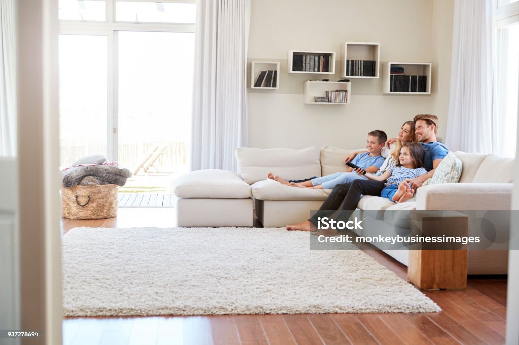 Family Sitting On Sofa At Home Watching TV Together Family Stock Photo