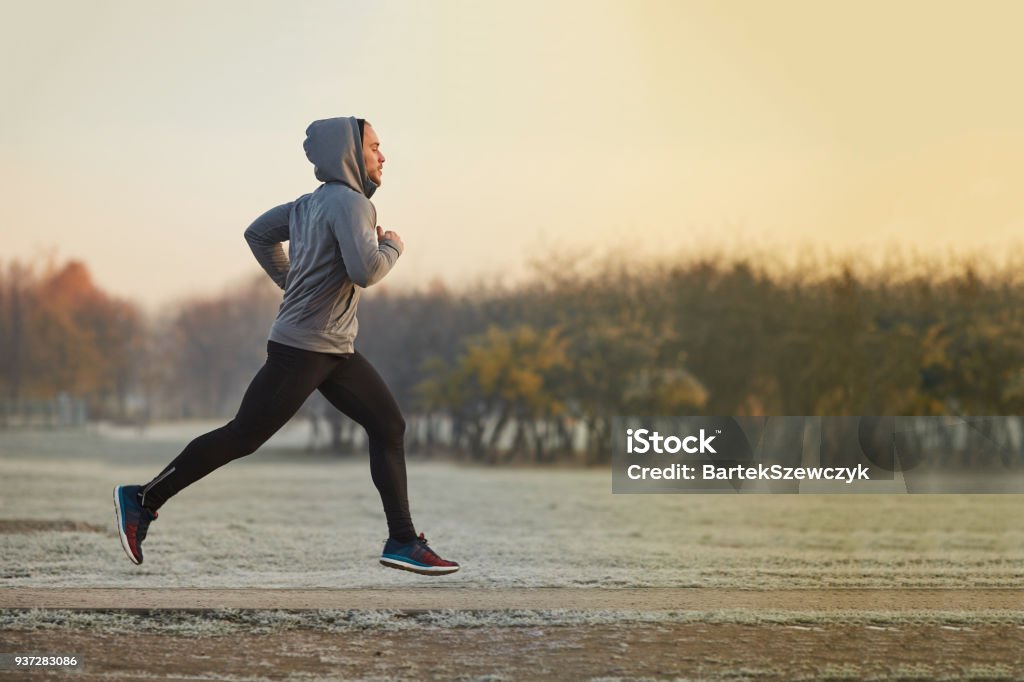 Joven atlético corriendo en el parque durante la fría mañana de otoño - Foto de stock de Correr libre de derechos