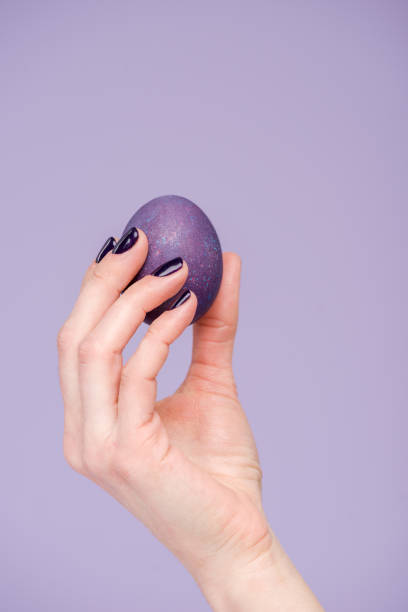 istock Female hand with purple Easter egg isolated on violet 937295340