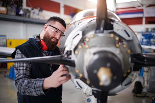 Male aircraft engineer in the hangar repairing and maintaining private jet airplane.