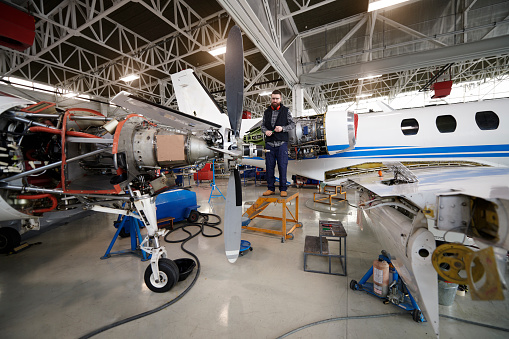 Male aircraft engineer in the hangar repairing and maintaining private jet airplane.