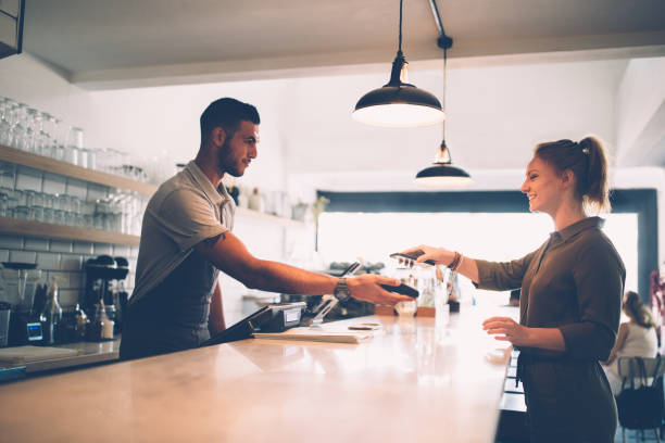 young woman making contactless payment with smartphone at cafe - coffee serving cafeteria worker checkout counter imagens e fotografias de stock