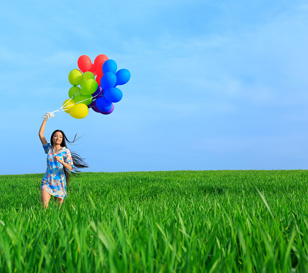 Cheerful young woman holding multicolored balloons and running