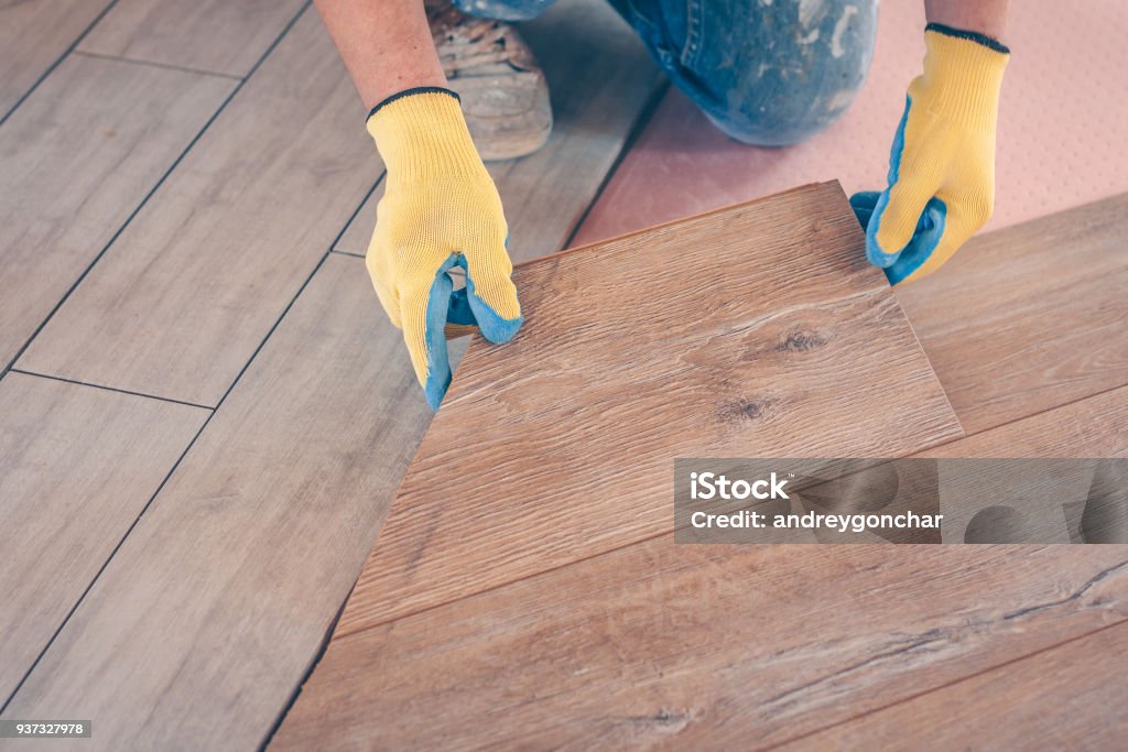 Professional installation of floor covering, the worker quickly and qualitatively mounts a laminate board Adult Stock Photo