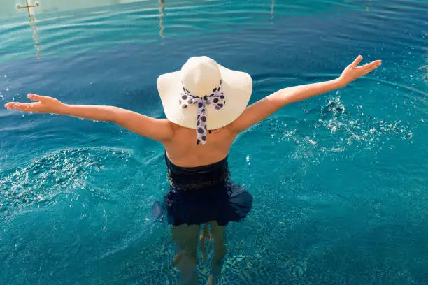 Asian woman relaxing in swimming pool with sunbathe.