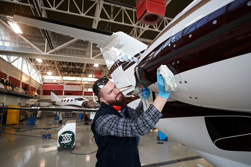 Male aircraft engineer in the hangar cleaning the private jet airplane.