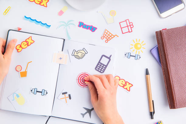 istock Female hand pinning clerical button on target icon in personal planning organizer among other icons of actions on the working place with stationery. Concept of planning and goals achievements in life. 937363522