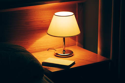 Book and vintage lamp on night table in hotel room. Retro styled bedroom interior.