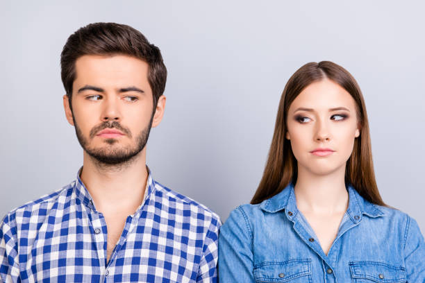 mistrust and cheat problems. annoyed couple is ignoring each other, but spy each other secretly, they stand on pure background in casual shirts - olhar de lado imagens e fotografias de stock