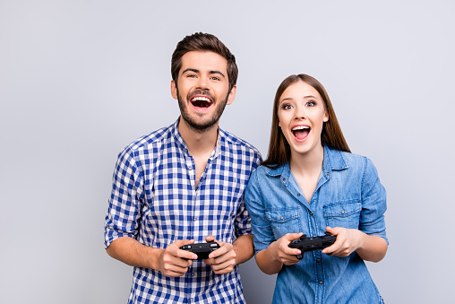 Goal! Yes! Married young people are fans of video games, love spending their weekend together. They stand on light background, in casual shirts