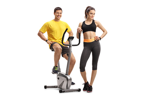 Young man on an exercise bike with a young woman isolated on white background