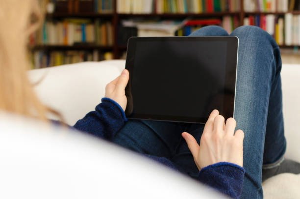 istock Woman is sitting in a domestic room and is looking at a blank tablet computer screen with copy space 937406546