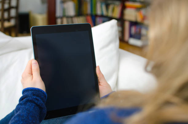 istock Woman is sitting in a domestic room and is looking at a blank tablet computer screen with copy space 937406592