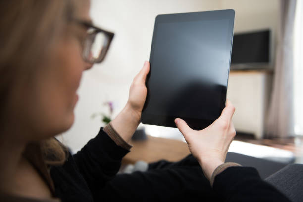 istock Woman with glasses is looking at a blank tablet computer screen with copy space 937407018
