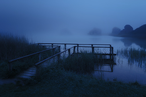 Dark landscape with mysterious wooden jetty on lake at night