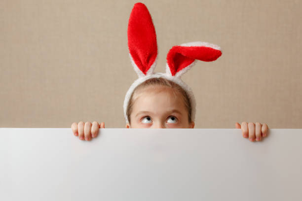 istock A nice little girl is looking because of an empty banner in which you can insert any text. 937414982