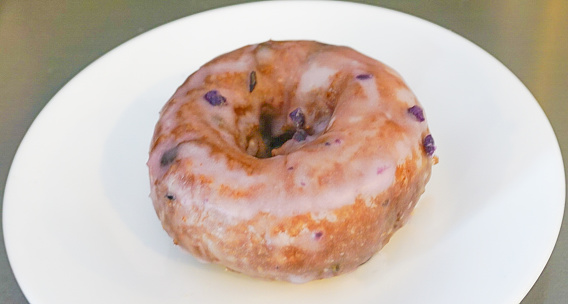 An up-close view of a blueberry cake doughnut with icing served on a white plate
