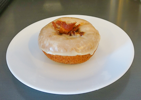An up-close view of a maple glazed bacon cake  doughnut served on a white plate
