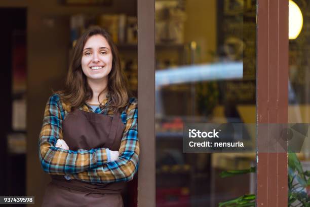 Beautiful Young Saleswoman Looking At Camera And Leaning Against The Door Frame Of An Organic Store Stock Photo - Download Image Now