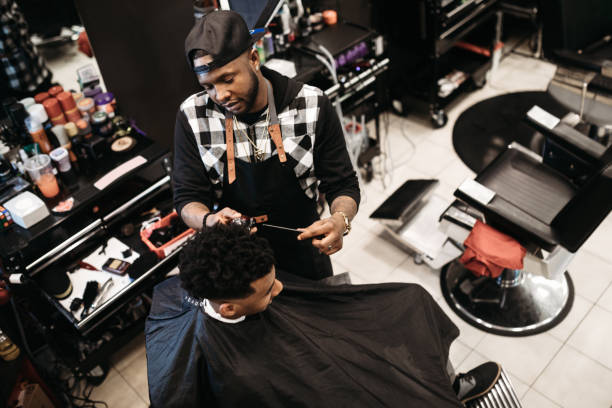 Barber Giving A Haircut in His Shop An African American man gets his hair cut by a skilled stylist at a small business barbershop. black barber stock pictures, royalty-free photos & images