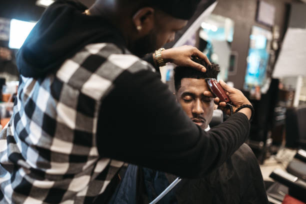 Barber Giving A Haircut in His Shop An African American man gets his hair cut by a skilled stylist at a small business barbershop. black barber stock pictures, royalty-free photos & images