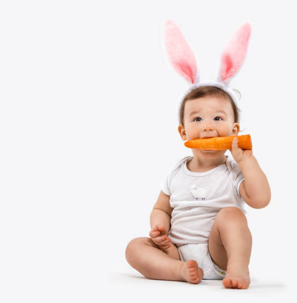 portrait d’un enfant dans un costume de lapin avec une carotte dans ses mains. photo à l’intérieur - baby carrot photos et images de collection