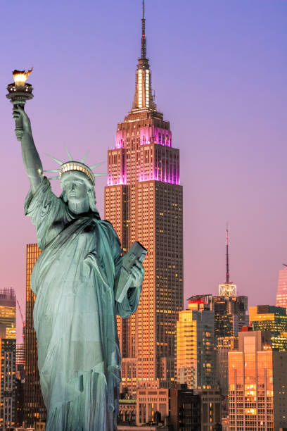 estatua de la libertad en la puesta del sol y el horizonte de nueva york con el empire state building, rascacielos de midtown manhattan y naranja-azul cielo claro. - clear sky vacations vertical saturated color fotografías e imágenes de stock