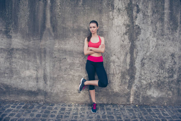istock Young serious slim trainer is stretching her leg by doing exercise. She is training outdoors on a summer day, wearing fashionable sport wear, sneakers, with pony tail 937510904