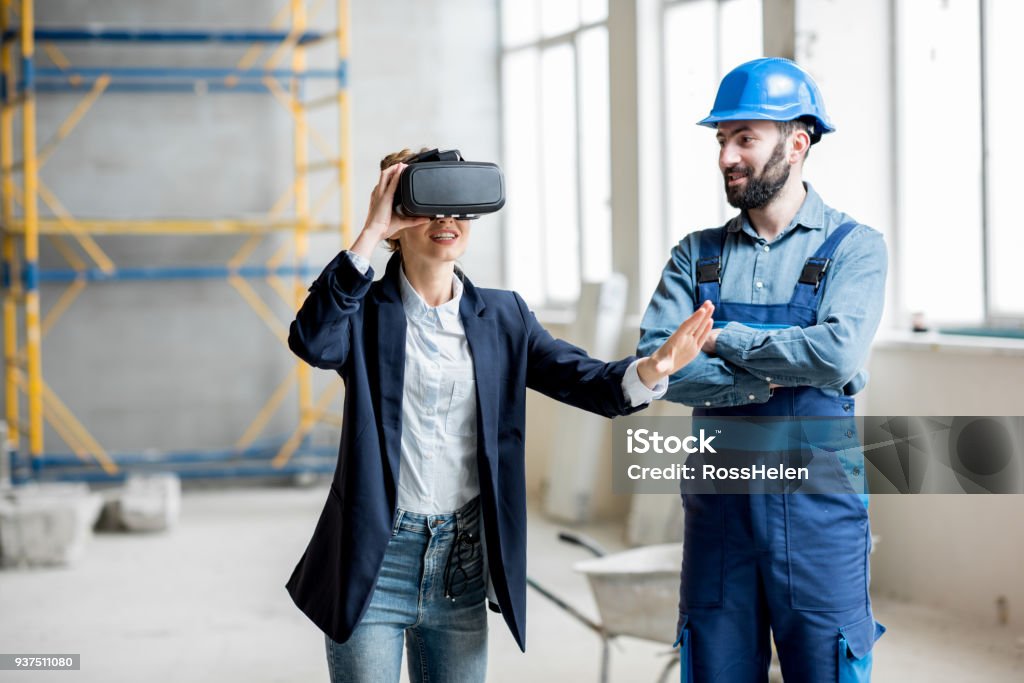 Woman client wearing VR glasses at the construction site Woman client wearing VR glasses imagining future interior standing with builder at the construction site Virtual Reality Stock Photo