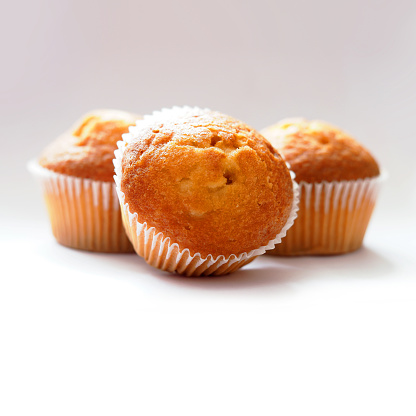 Freshly baked muffins. Three muffins in wax liner on light background. Small biscuit tasty cupcakes, delicious