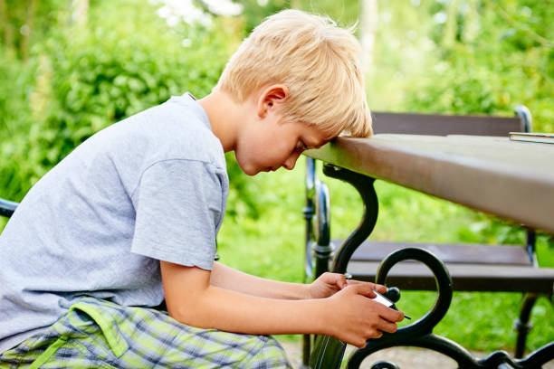 istock Child boy sitting on a bench and playing game with smartphone 937539858