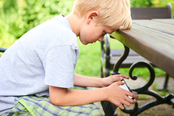istock Child boy sitting on a bench and playing game with smartphone 937539864