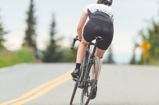 weibliche radfahrer fährt entlang einer ländlichen autobahn - cyclist cycling road women stock-fotos und bilder