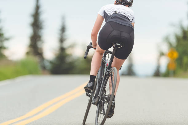 ciclista pedala lungo un'autostrada rurale - cyclist cycling road women foto e immagini stock